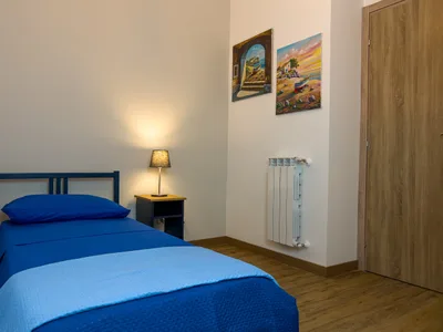 Camera singola con letto in legno blu, biancheria azzurra, comodino e quadri alle pareti