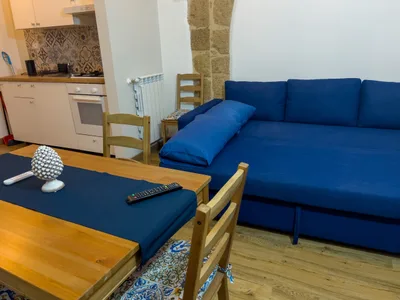 Vista del soggiorno con tavolo da pranzo, divano letto blu e cucina attrezzata