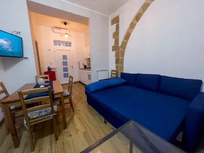 Panoramica del soggiorno con TV a parete, zona pranzo, divano letto e arco in pietra