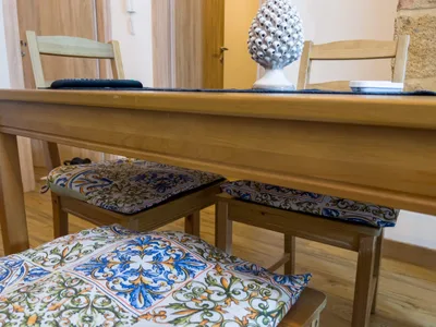 Dettaglio del tavolo da pranzo con pigna in ceramica e cuscini decorati in stile siciliano